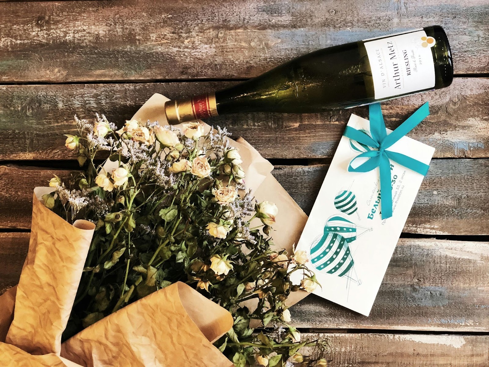 A wine bottle, a card and a bouquet laying on a wooden platform