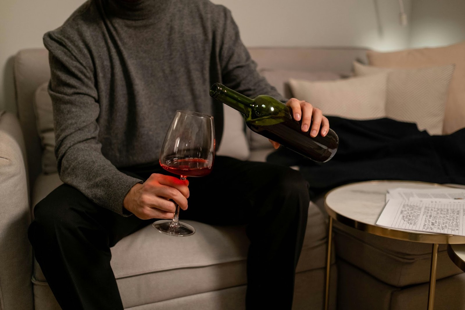 A man sitting on couch and pouring red wine in his glass