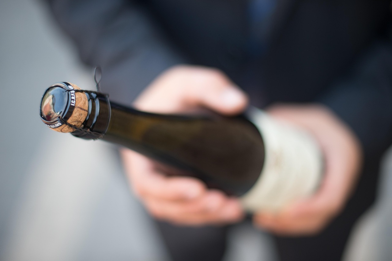 A man holding a bottle of wine blurred in background and the closed lid of that bottle in focus