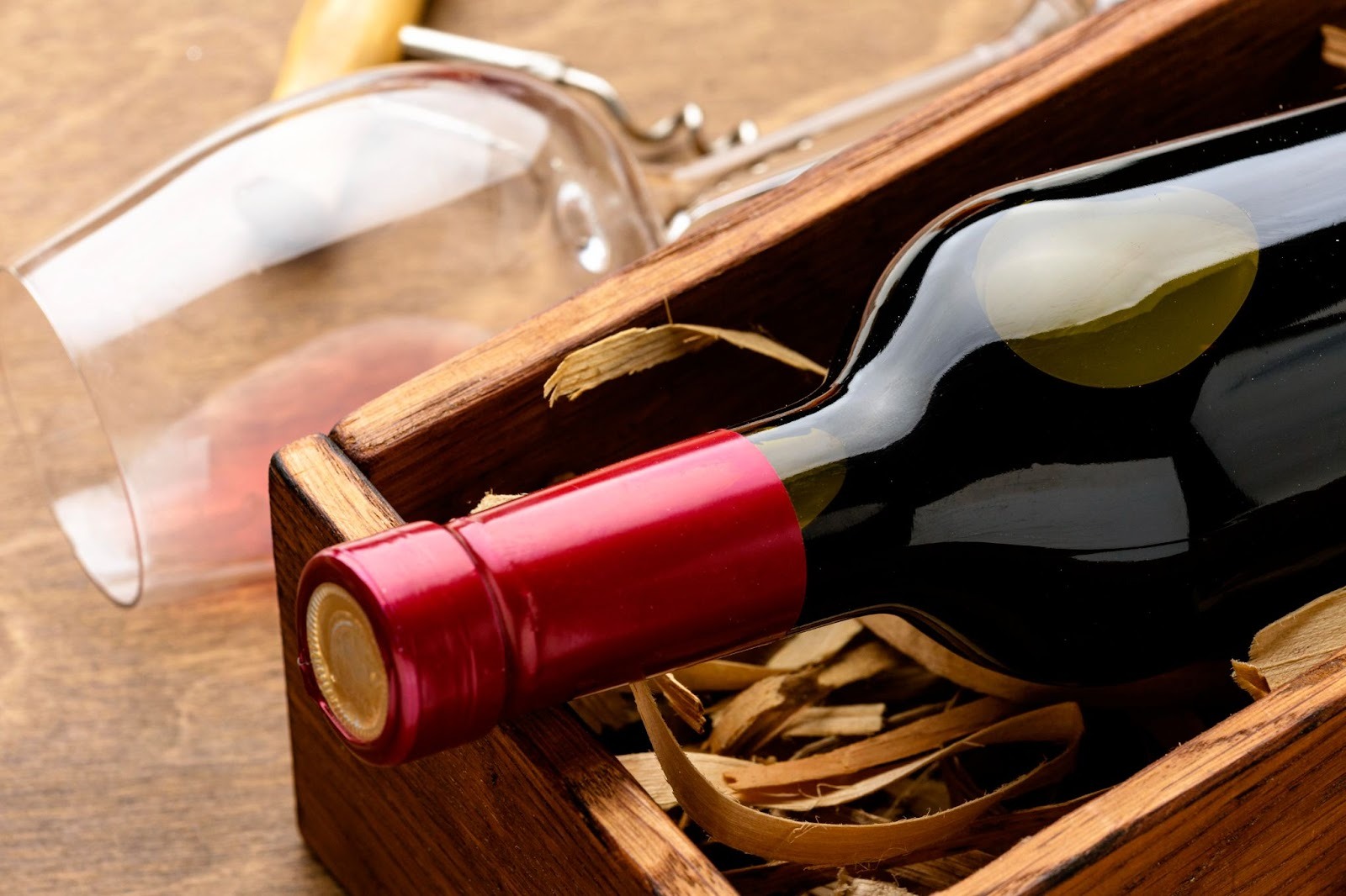 Wine bottle in a wooden container and a glass and a cork screw near it