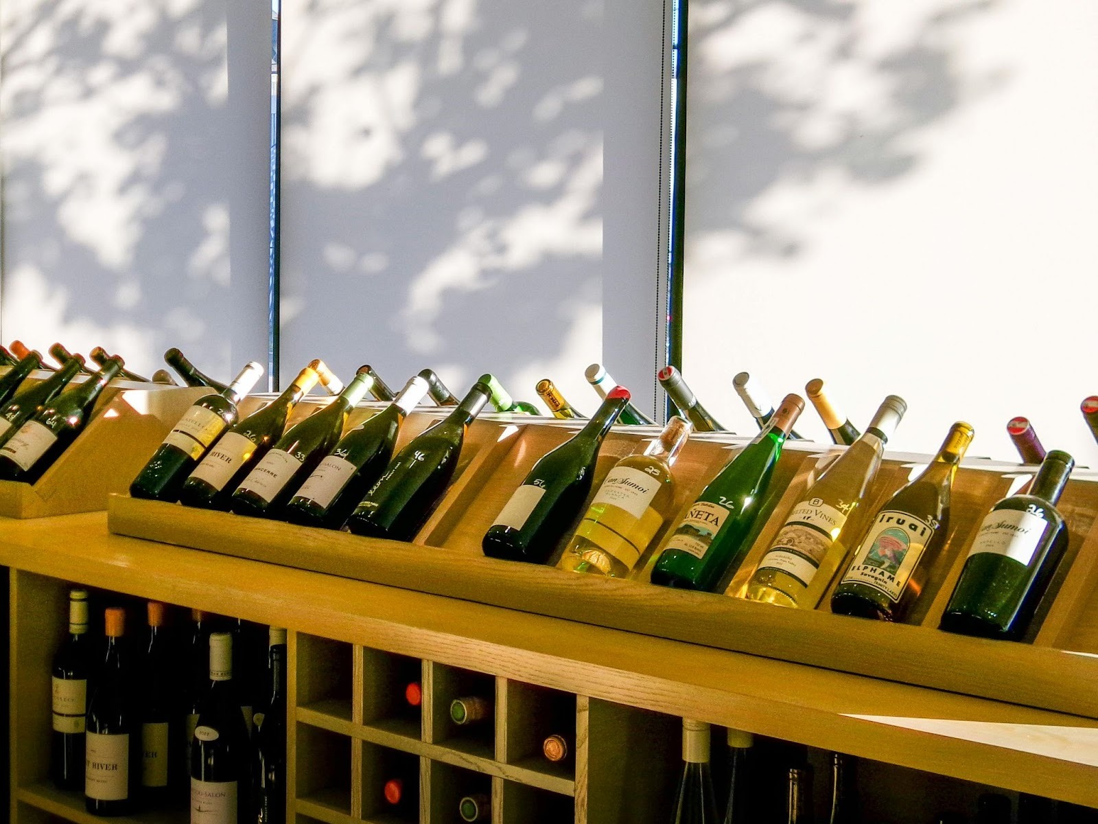 Wine bottles in a wooden cabinet near window and sunlight falling on them