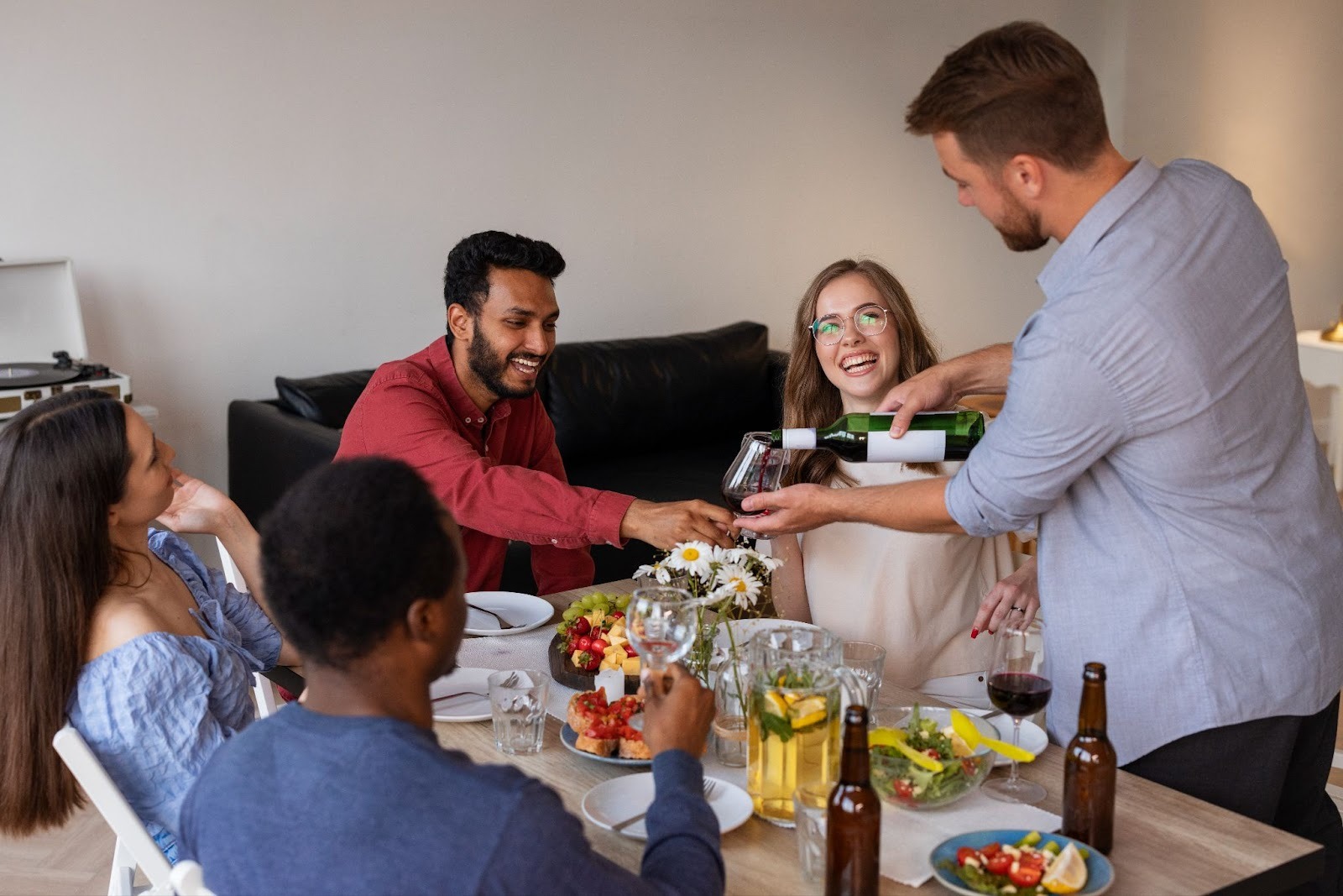 Five friends gathered dinner at home and one serving wine while others are sitting around table