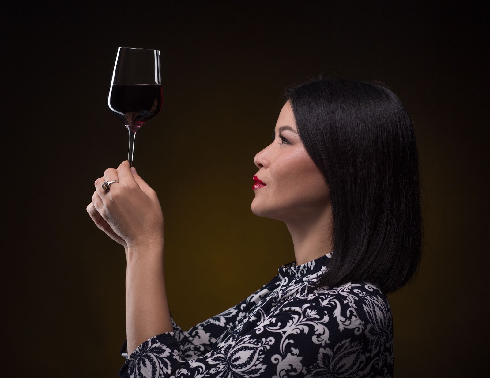 Asian sommelier woman looking at a glass of red wine in her hand very attentively