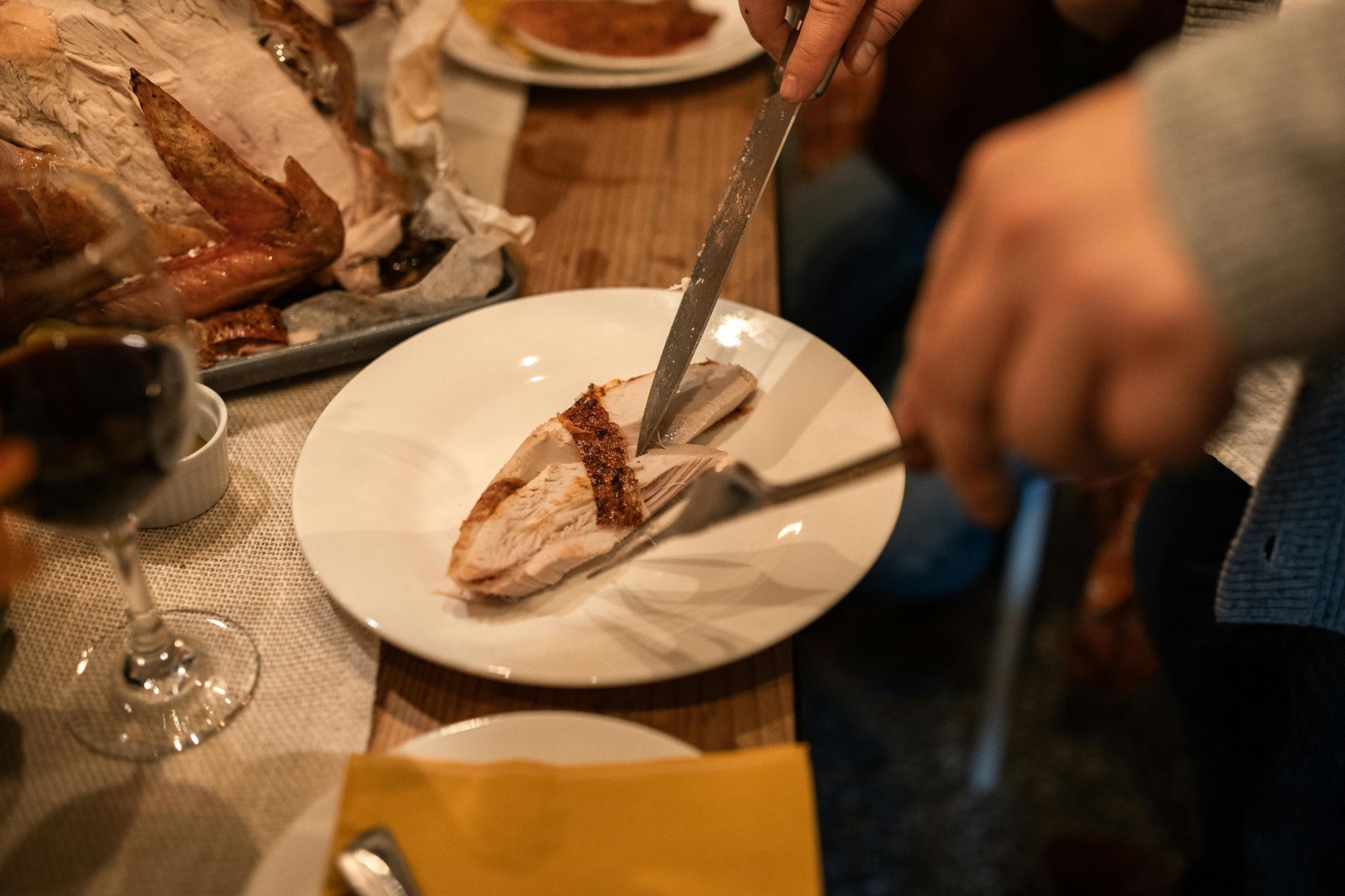 A man cutting steak in his plate with a wine glass nearby