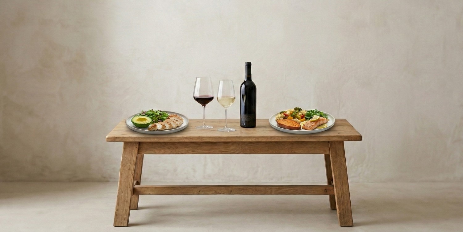 A glass of red and a white wine next to a bottle on a wooden table; a plate of keto-friendly foods on either sides