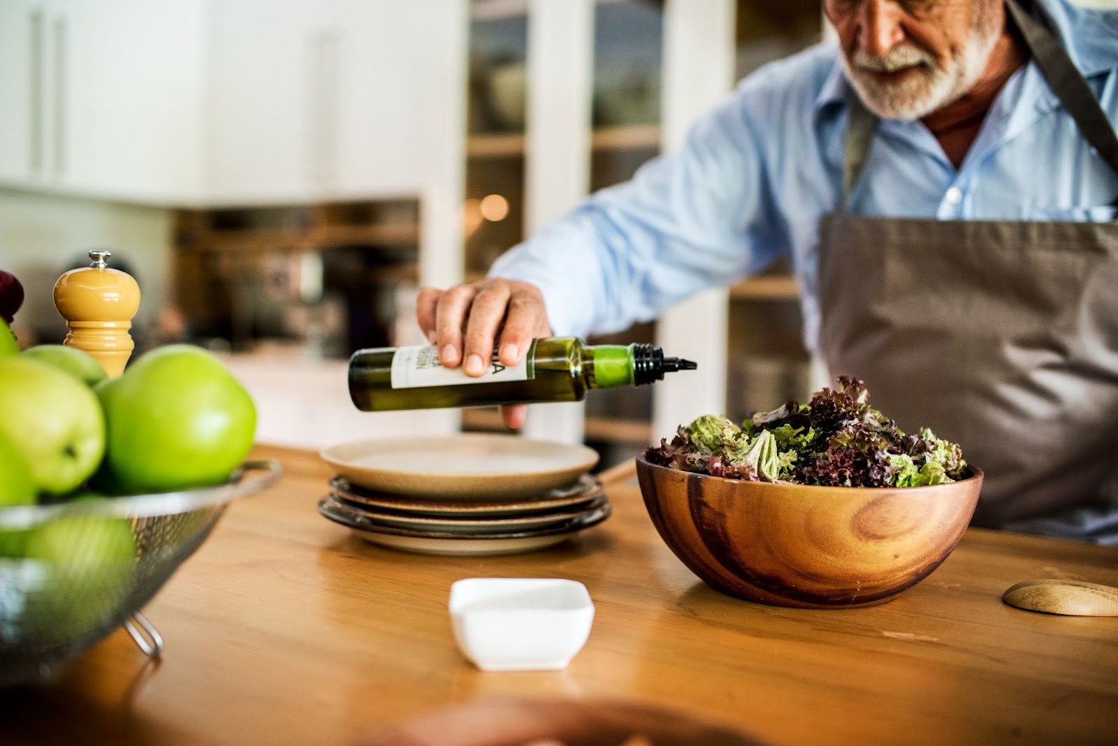 An old man pouring wine into a bowl of vegetables on kitchen table
