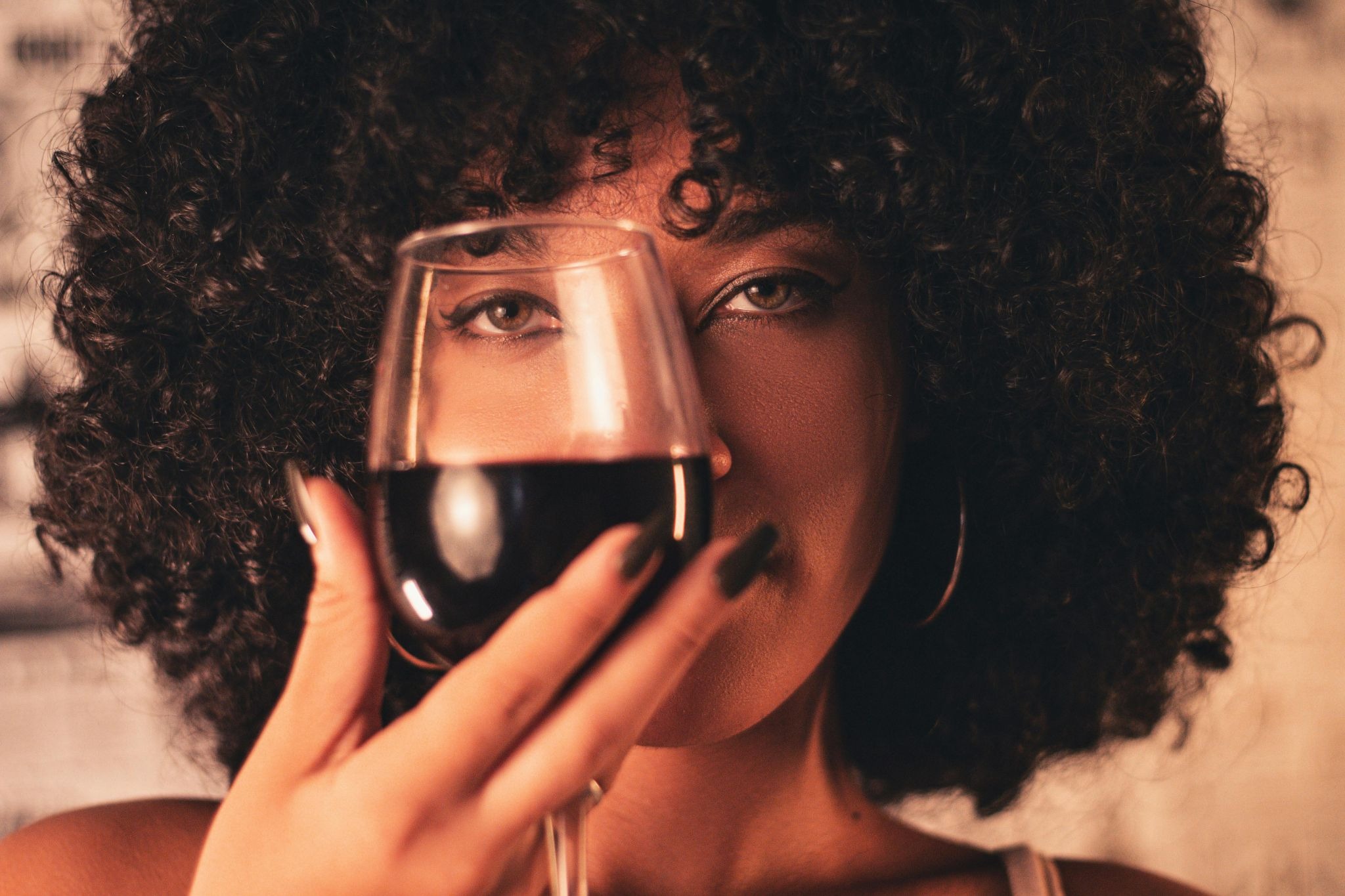 a woman holding red wine glass beside her eye to look through