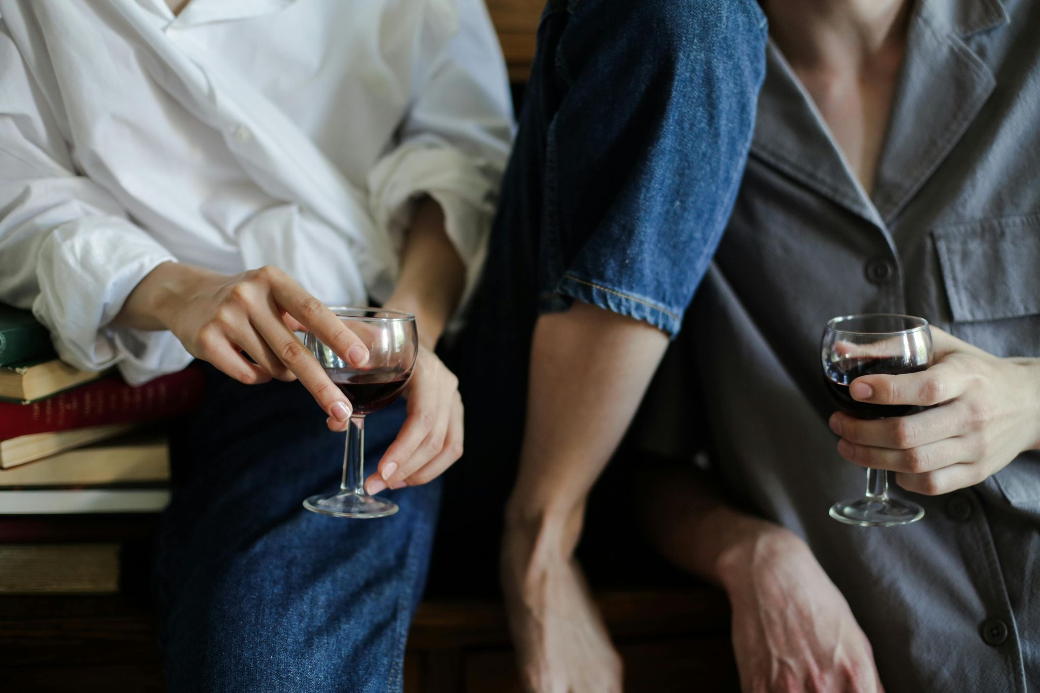 two people holding red wine glass one sitting casually on table and other leaning on table