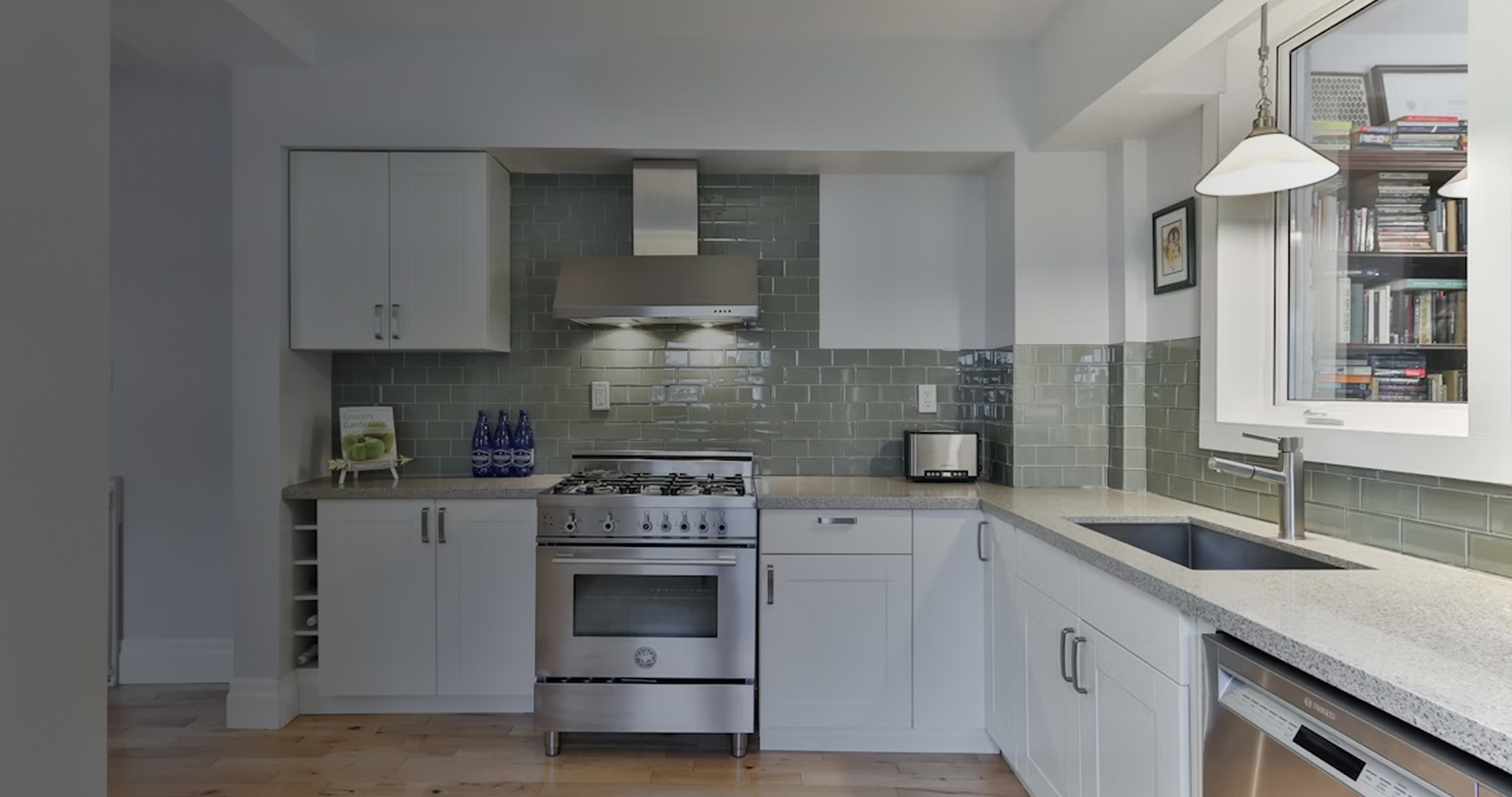 Modern kitchen with stainless steel stove, gray subway tile backsplash, white cabinets, and a window over the sink.