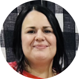 Smiling woman with long black hair and light skin wearing a red top against a checkered black and white background.