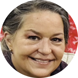 Smiling middle-aged woman with light skin and dark hair pulled back, wearing small earrings.