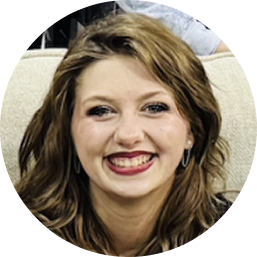 Smiling young woman with wavy brown hair, wearing hoop earrings, sitting on a beige couch.