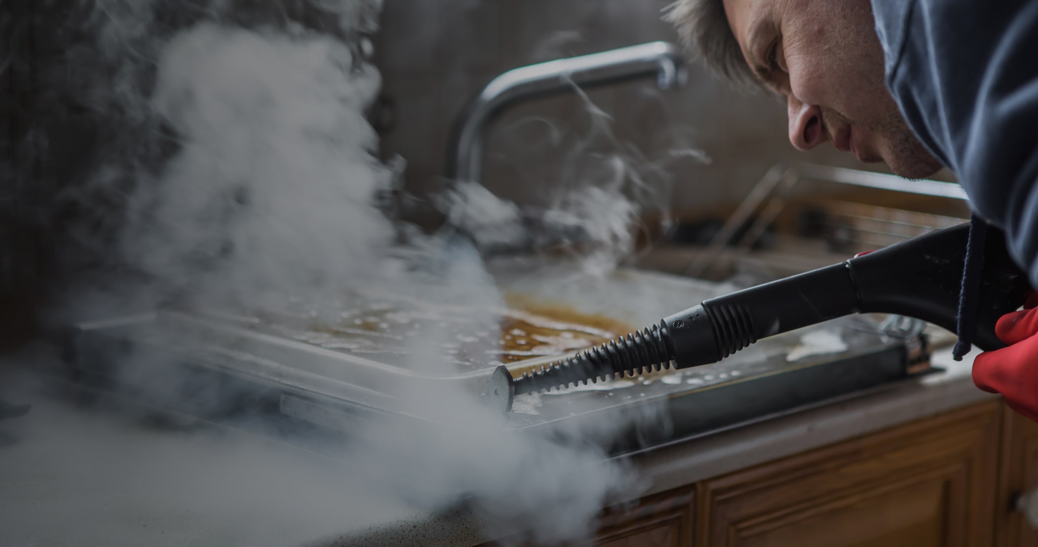 Person using a steam cleaner to clean a greasy oven tray in a kitchen.