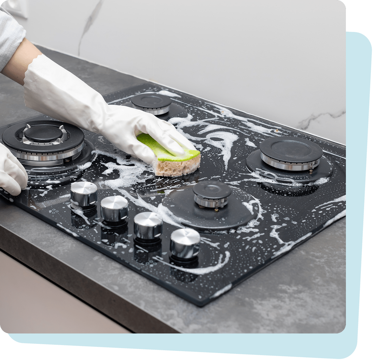 Person wearing white gloves cleaning a black gas stove with a green sponge and soap suds.