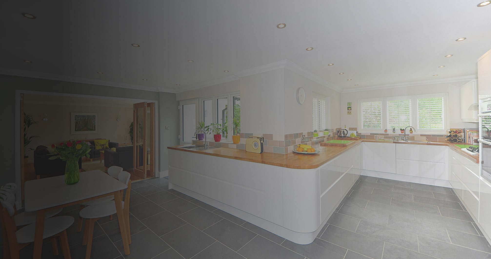 Modern kitchen with white cabinets, wooden countertops, gray tile floor, and multiple windows with white shutters.