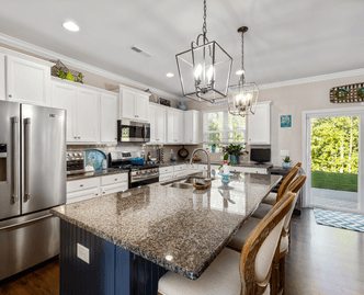 Modern kitchen with a large granite island, stainless steel appliances, white cabinetry, and two pendant lights above the island with wooden bar stools.