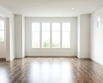 Empty room with white walls, large windows, and polished wooden floor reflecting light.