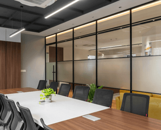 Modern conference room with a long table, black mesh chairs, potted plants, and frosted glass partitions.