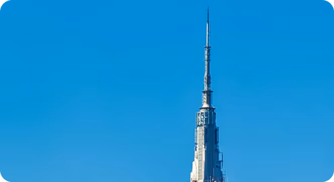 Top portion of a tall skyscraper with an antenna against a clear blue sky.