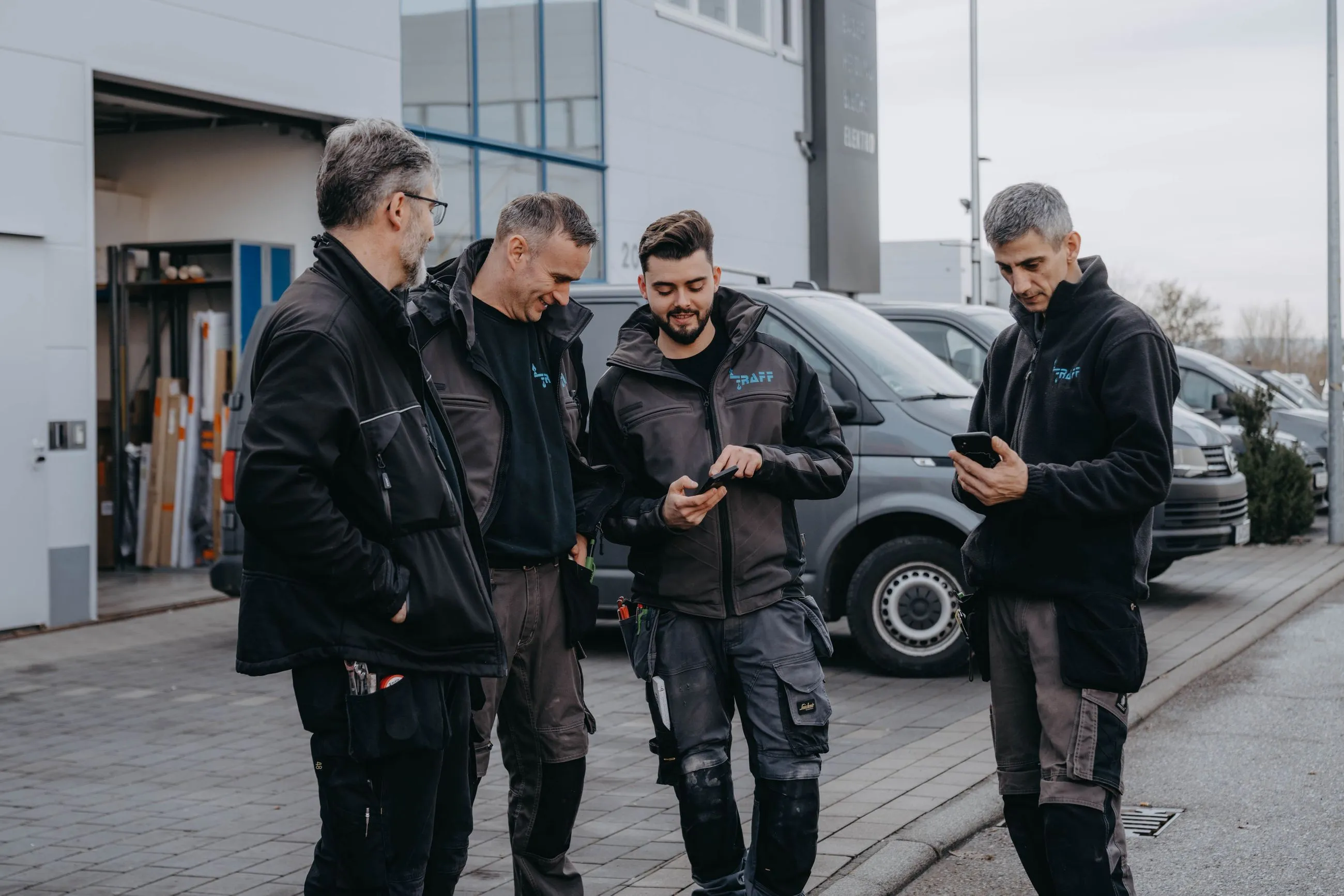 Vier Handwerker besprechen sich vor Firmenfahrzeugen.