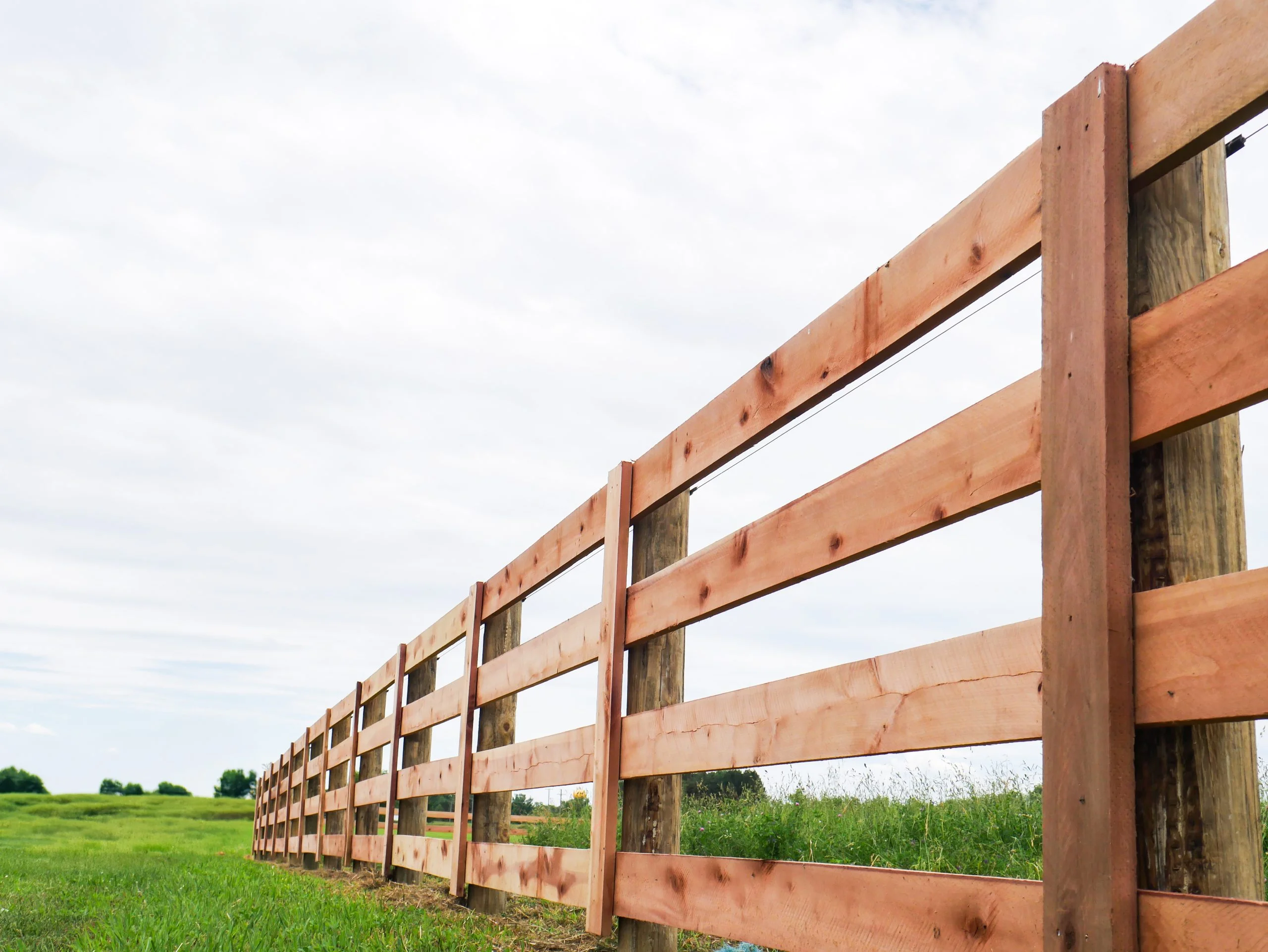 Long wooden fence stretching across a grassy pasture under a cloudy sky.