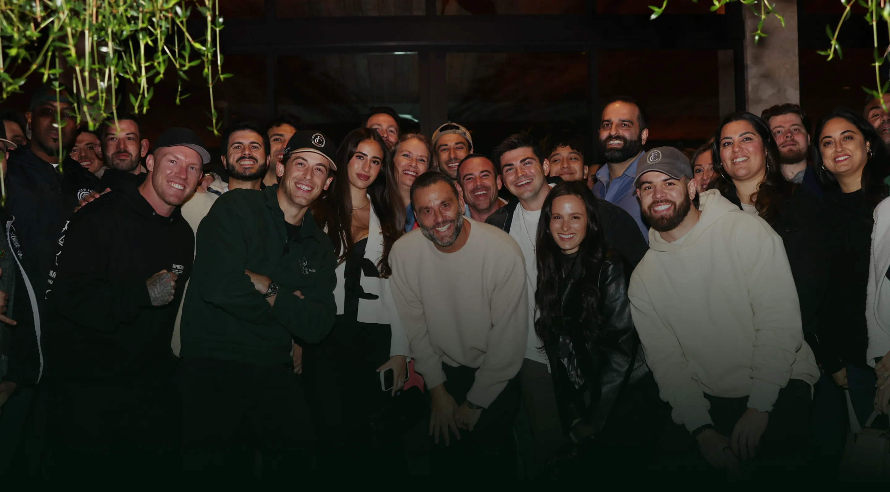 Group of smiling young adults posing together outdoors at night under canopy tents.