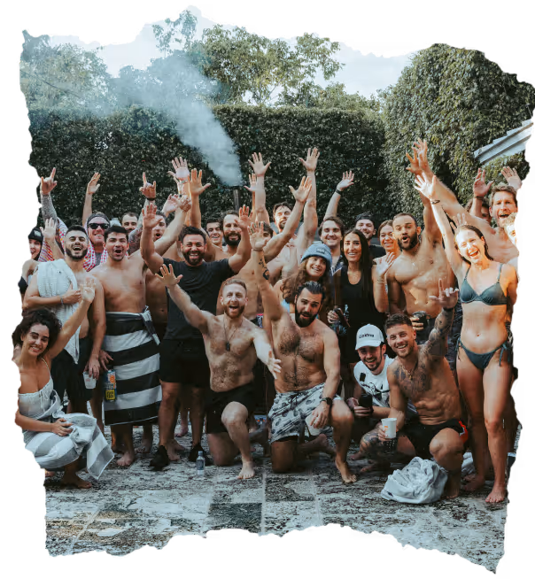 Group of young adults in swimwear and casual clothes smiling and raising hands outdoors, celebrating together.