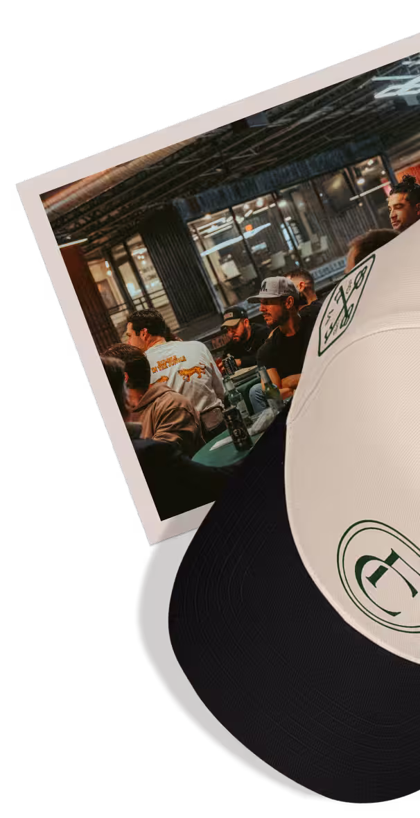 Group of young adults socializing indoors, some holding drinks, with large glass windows and outdoor patio visible.