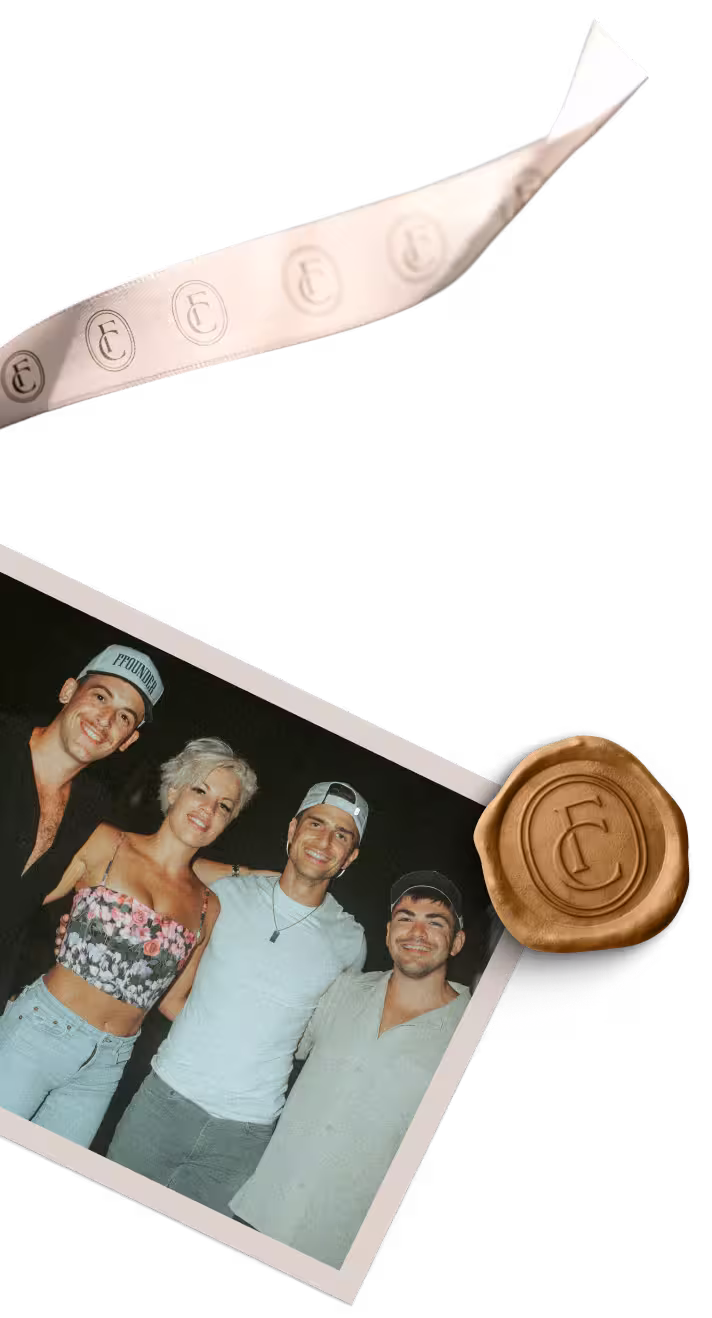 Outdoor dining area at dusk with string lights hanging above tables and chairs surrounded by palm trees.