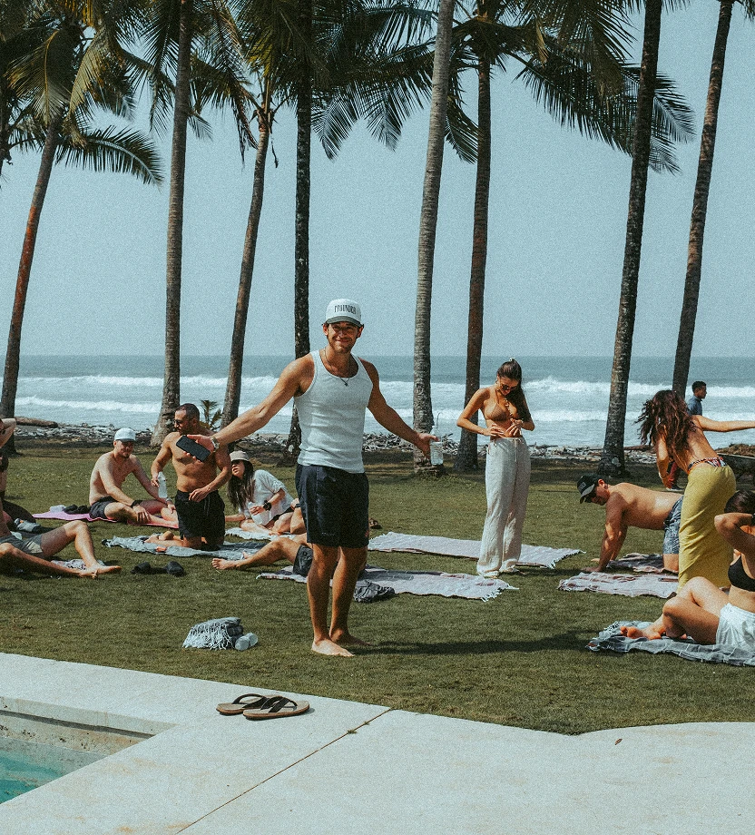Group of young adults posing shirtless and in swimwear outdoors, with lush green foliage in the background.