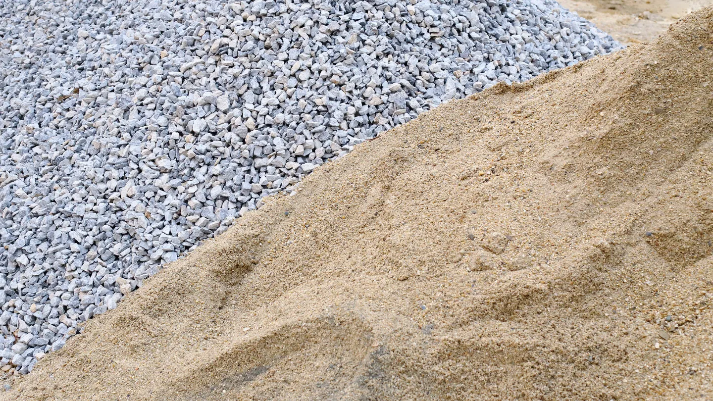 Piles of coarse gray gravel and fine beige sand at a construction site.
