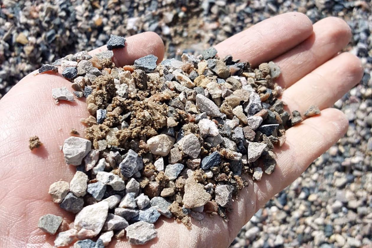 Hand holding a handful of small mixed gravel and soil particles outdoors.