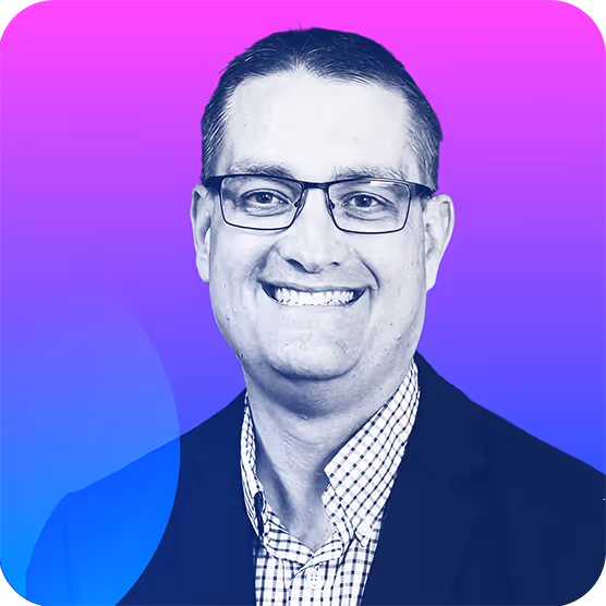 Smiling man wearing glasses and a checkered shirt under a dark blazer on a vibrant purple and blue gradient background.