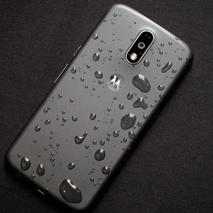 Motorola smartphone with water droplets on its back surface resting on a black fabric background.