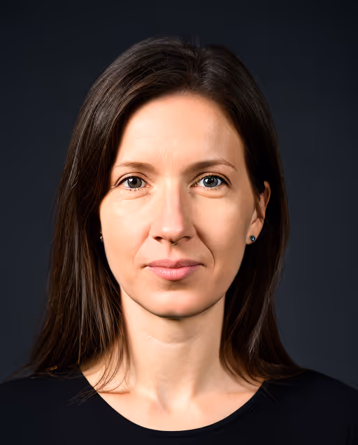 Portrait of a woman with long brown hair and blue eyes wearing a black top against a dark background.