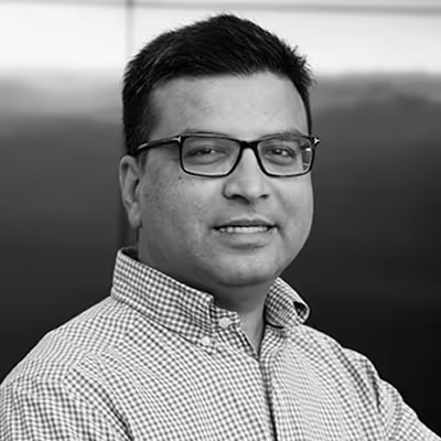 Man wearing glasses and a checkered shirt smiling, facing slightly to the side in a black and white portrait.