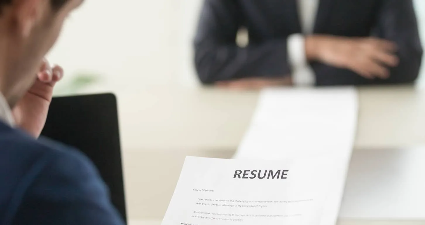 Person holding a resume in an interview with another person sitting across a table.