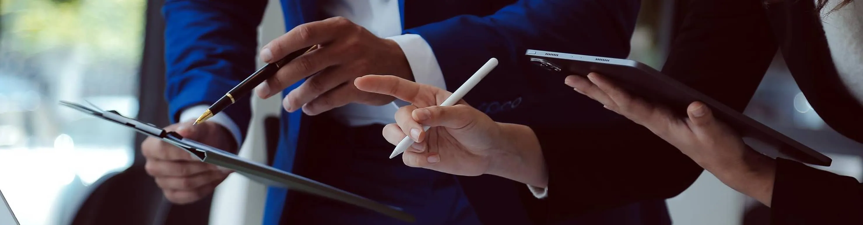 Close-up of three people's hands using digital tablets and a pen in a business meeting.