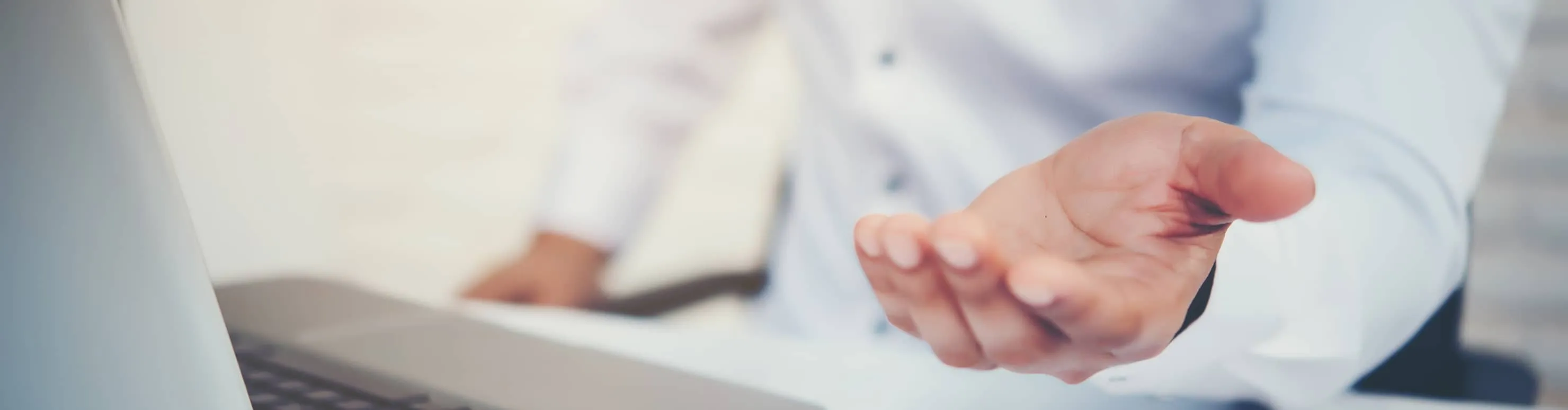 Open hand gesture extended towards the viewer with a laptop and person in blurred background.