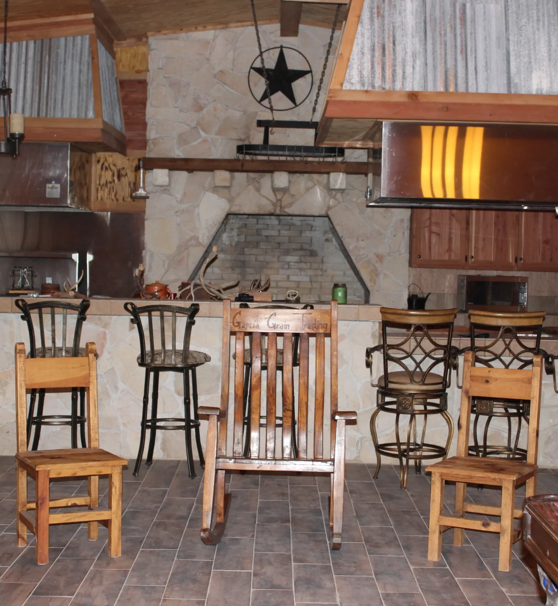 Rustic bar area with five chairs, including a wooden rocking chair, stone fireplace, and metal star wall decor.