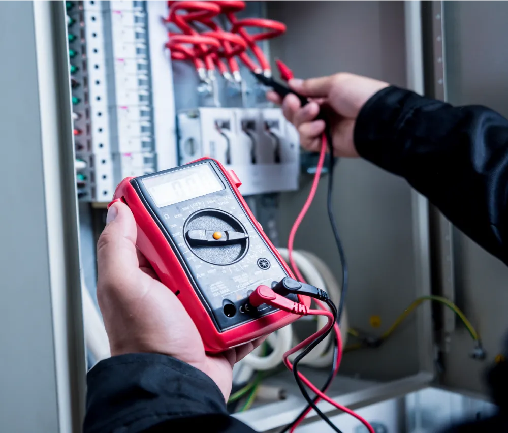 Person holding a digital multimeter testing electrical connections in a circuit breaker panel.