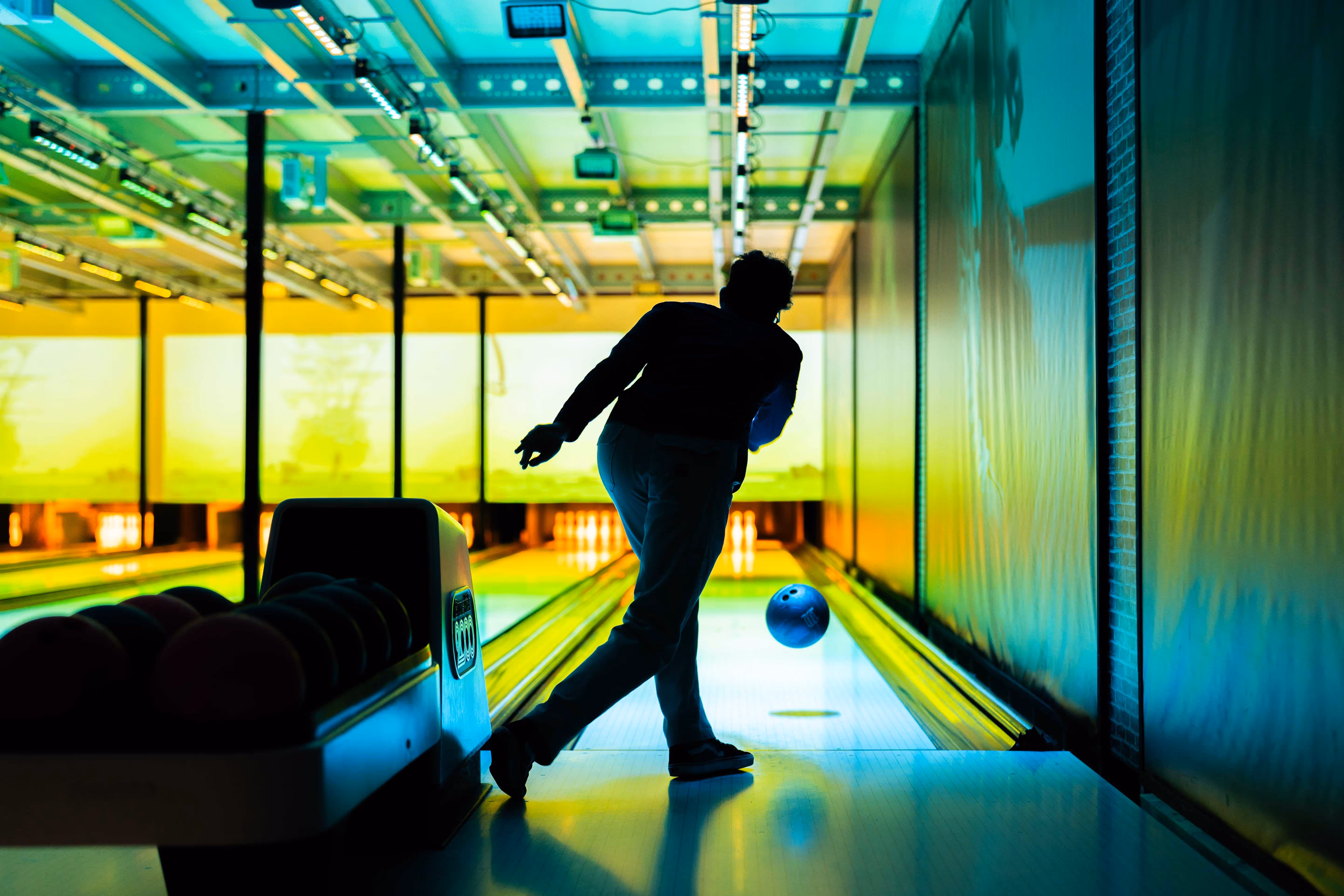 Silhouet van een persoon die een bowlingbal werpt in een fel verlichte bowlingbaan.