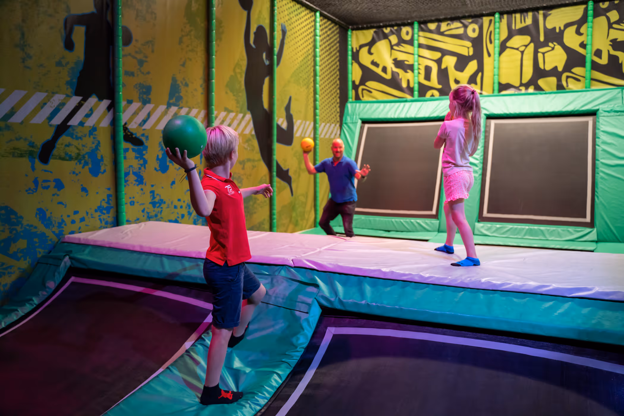 Drie mensen spelen trefbal op trampolinebanen in een indoor trampolinepark.