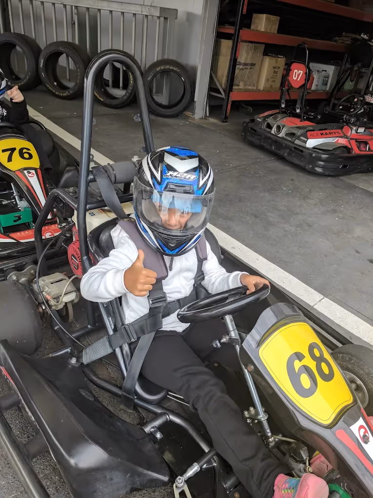 Child wearing a helmet gives a thumbs up while sitting in go-kart number 68 at Ace Karts.
