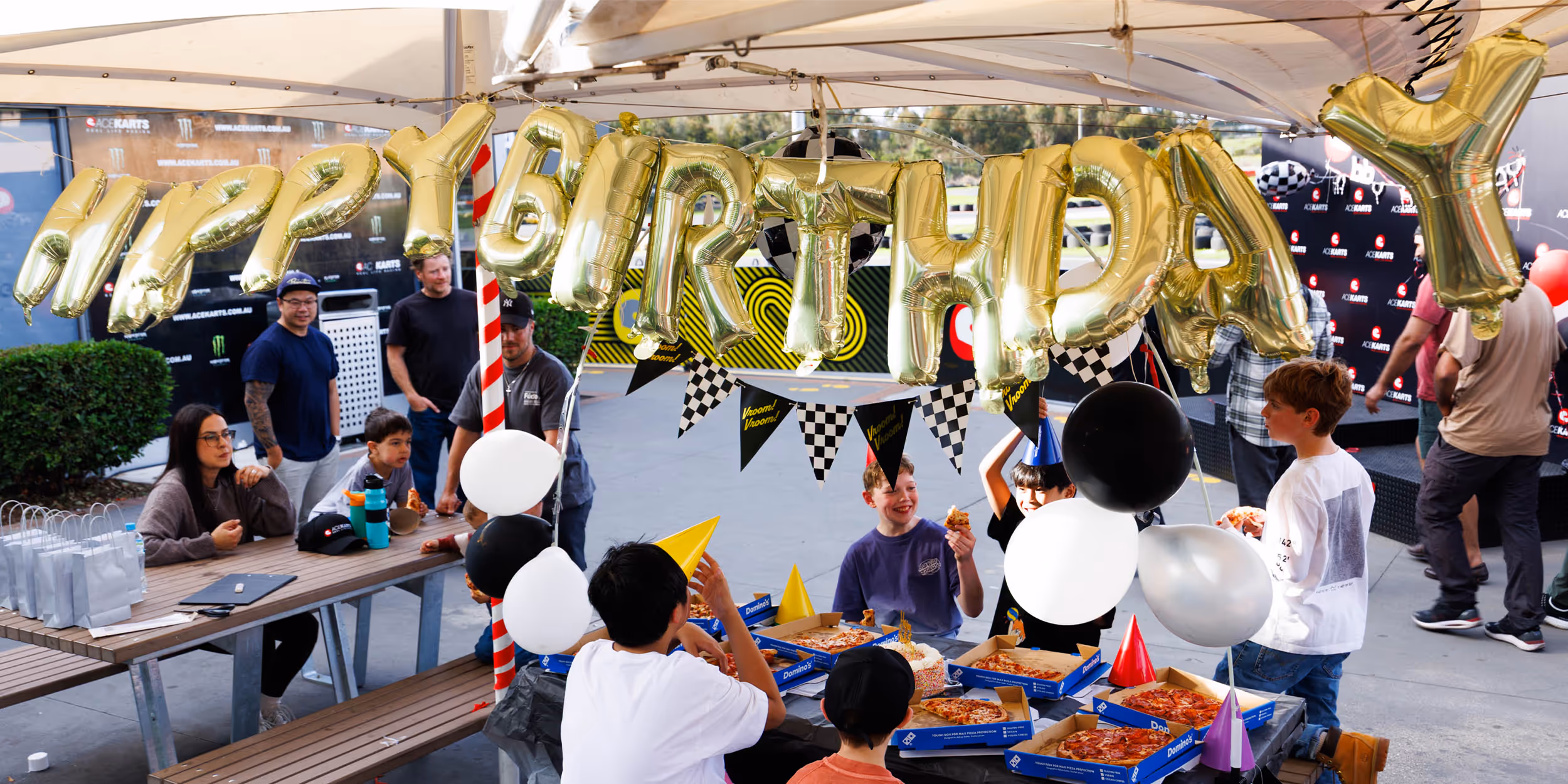 Birthday party group in helmets at Ace Karts beside the outdoor track.