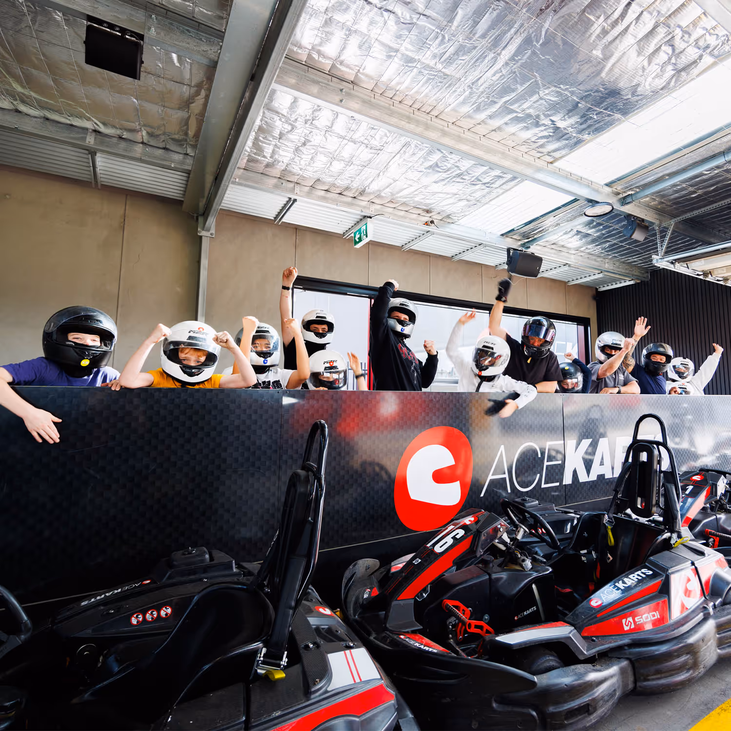 Young racer holding a helmet at Ace Karts with the pit area in the background.