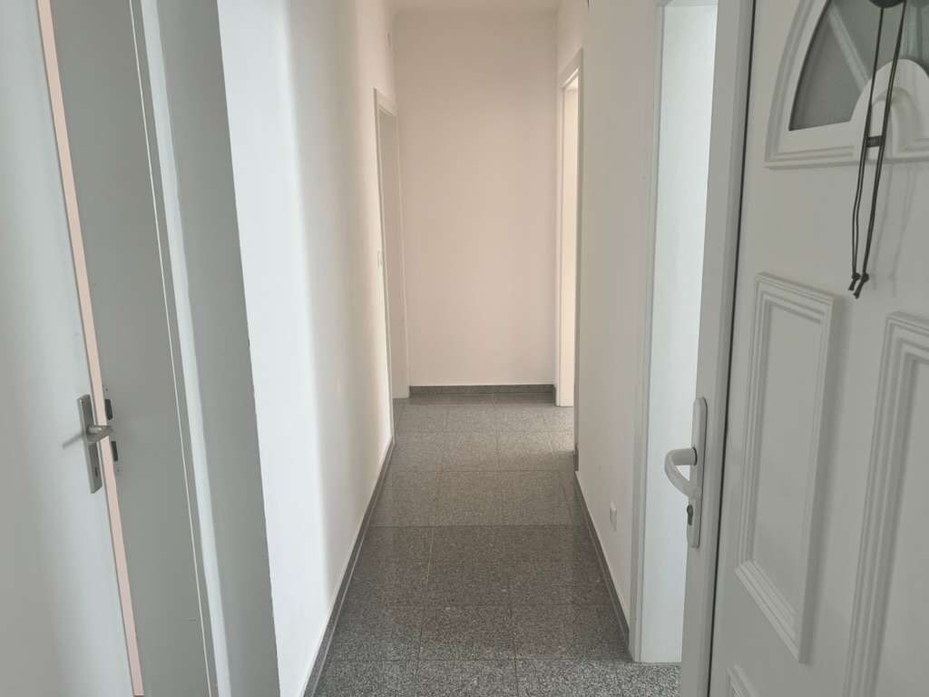 Schlichter Flur mit grauem Bodenbelag, weißen Wänden und mehreren Türrahmen