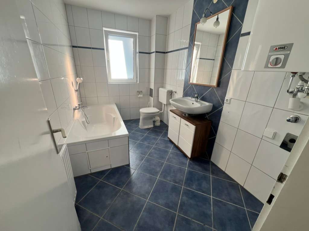 Helles Badezimmer mit Badewanne, WC, Waschbecken und blauem Fliesenboden