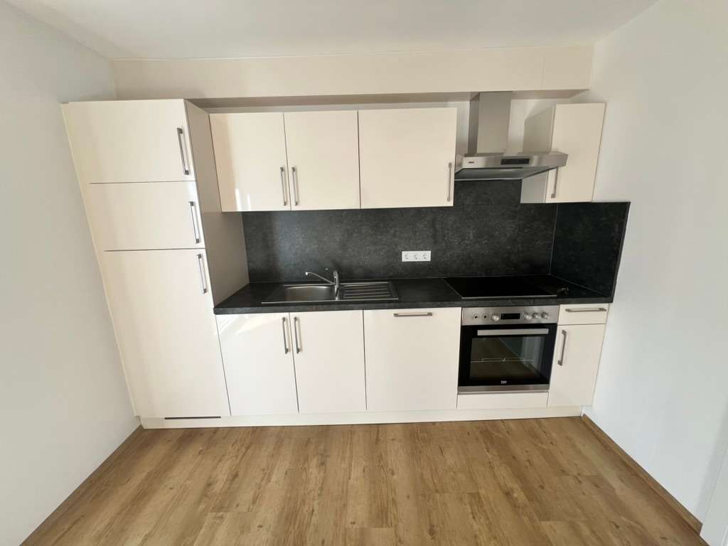 Moderne kompakte Einbauküche mit weißen Hochglanzfronten und dunkler Arbeitsfläche