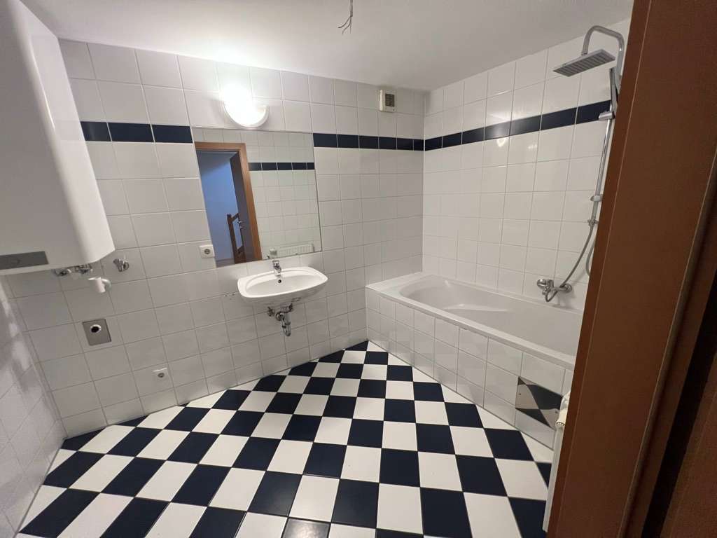 Badezimmer mit Badewanne, Waschtisch und schwarz-weiß kariertem Fliesenboden